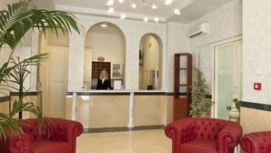 A lobby with a reception desk, red leather sofas, and a large potted plant. - Hotel Pai (Torri del Benaco)