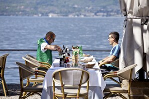 A table set for two at a waterfront restaurant with wicker chairs and a view of the sea. - Hotel Pai (Torri del Benaco)