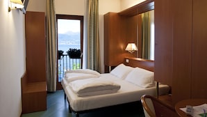 A hotel room with a bed, a desk, a chair, a window with curtains, and a view of the mountains. - Hotel Pai (Torri del Benaco)