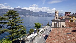 A coastal town with a prominent church featuring a bell tower, a paved road, and a clear view of the sea and mountains in the background. - Hotel Pai (Torri del Benaco)