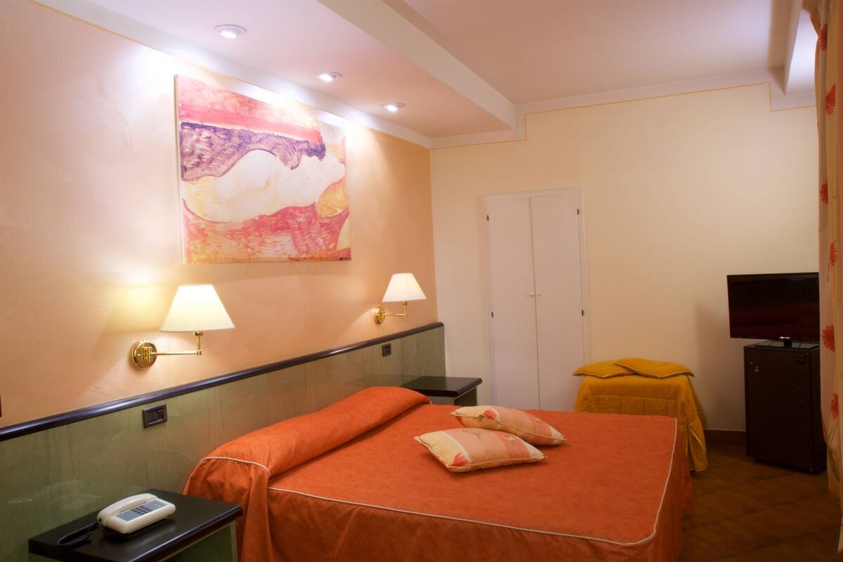 Une chambre d’hôtel avec un lit, des lampes de chevet, une télévision, une petite table et un tableau au mur.