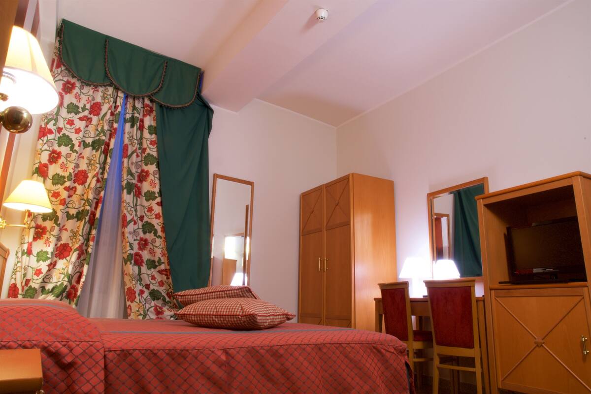 Une chambre d’hôtel comprenant un lit, une armoire, un bureau avec une chaise et un téléviseur.