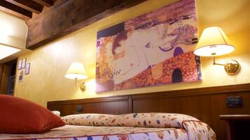 Habitación de hotel con cama, colcha estampada, dos lámparas fijadas a la pared y un cuadro grande sobre la cama.
