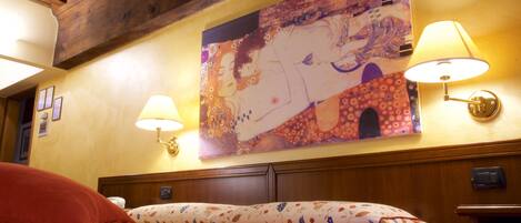 Een hotelkamer met een bed, een bloemenprint beddeken, twee wandlampen en een groot schilderij boven het bed.