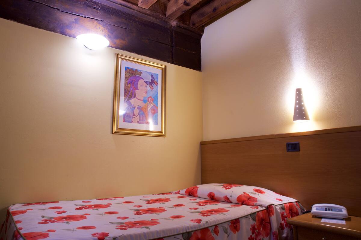 Un lit simple avec une couvre-lit à motifs floraux, un tableau encadré au mur et un téléphone sur la table de chevet.