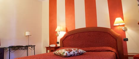 Habitación de hotel con una cama grande, paredes a rayas, dos lámparas de noche, una mesita pequeña y un escritorio.