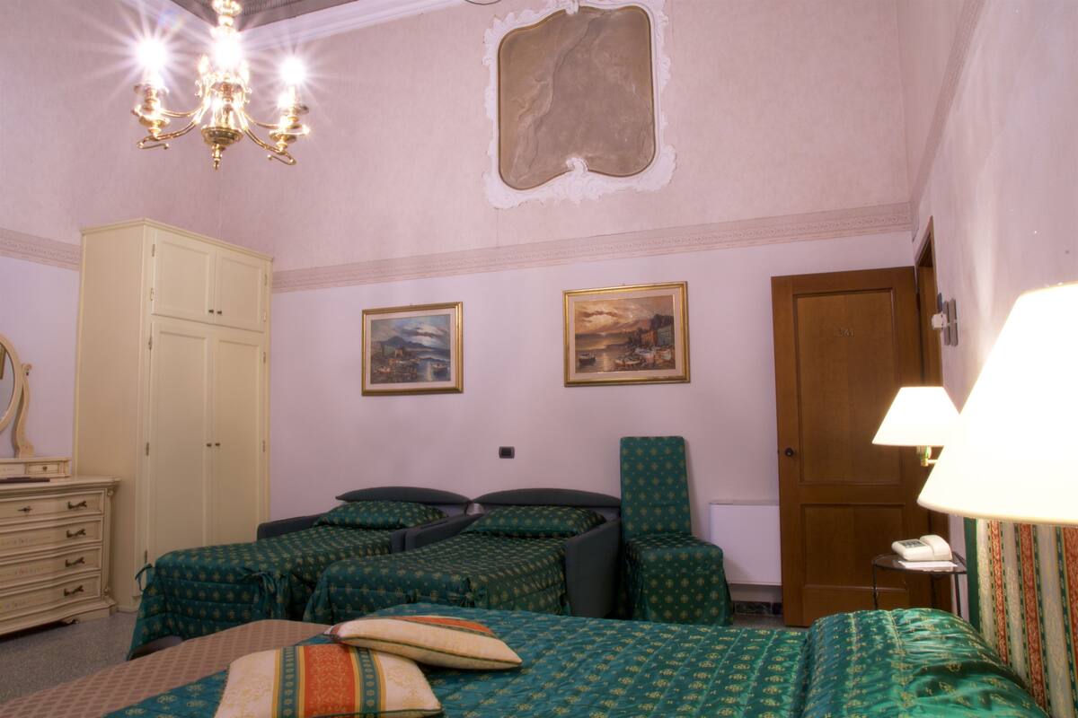 Une chambre d’hôtel avec deux lits simples, une armoire en bois, un lustre et deux tableaux encadrés au mur.