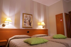 A hotel room with a large bed, two bedside lamps, a framed artwork on the wall, and a wooden door with a keycard lock.
