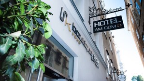 Ein Hotelschild mit dem Schriftzug "HOTEL AM DOM" und einem dekorativen hängenden Schild darüber.