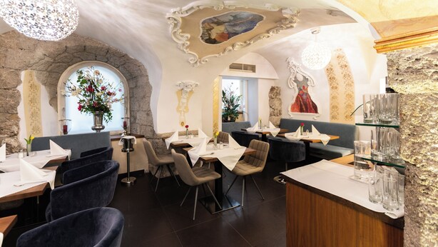 Ein Restaurant mit Steinwänden, Rundbogenfenstern und einer Chandelier. Tische sind mit weißen Tischdecken und Stühlen gedeckt.