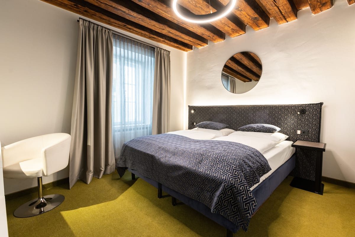 Una habitación de hotel moderna con una cama, una silla, un espejo redondo y una mesita de noche.