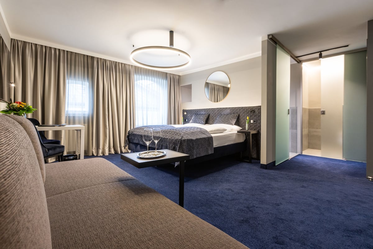Una habitación de hotel moderna con una cama grande, un sofá, una mesita con bandeja y un espejo amplio.