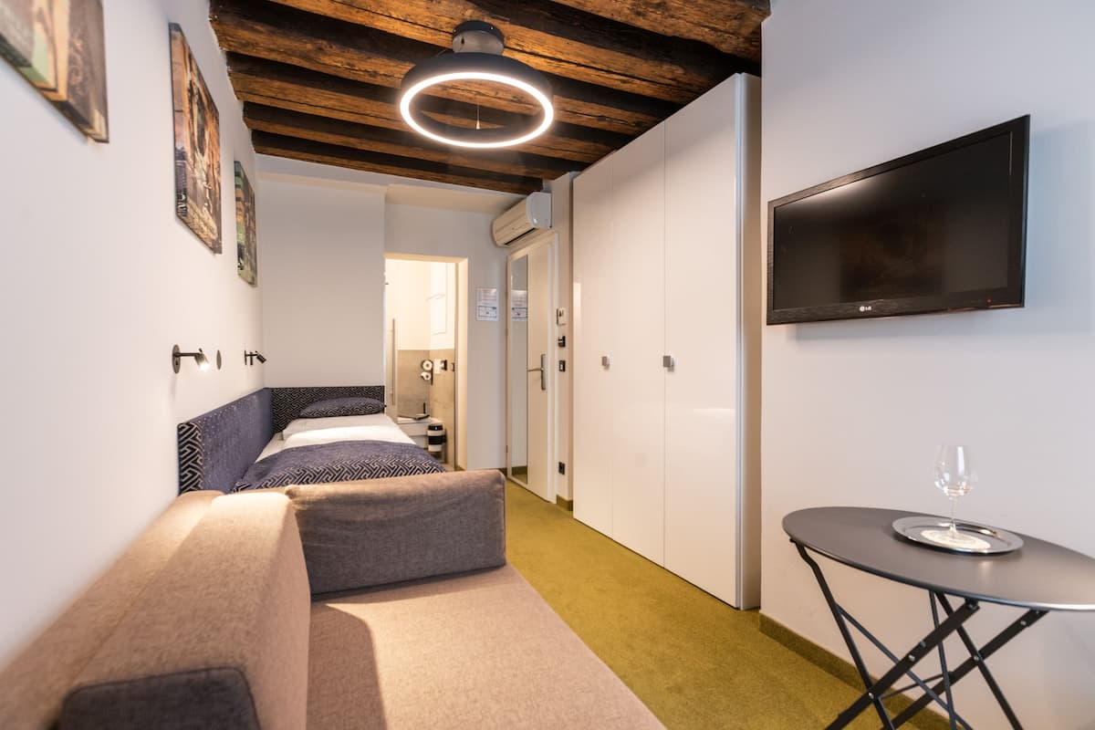 Una habitación de hotel moderna con una cama, una mesita con un vaso y un televisor en la pared.