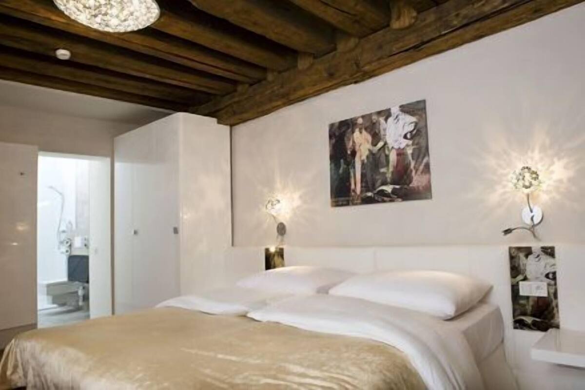 Un dormitorio con cama, vigas de madera en el techo, una lámpara fijada a la pared y un cuadro enmarcado.