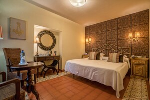 Quarto de hotel com uma cama grande, uma escrivaninha com cadeira, espelho e luminárias fixadas na parede.