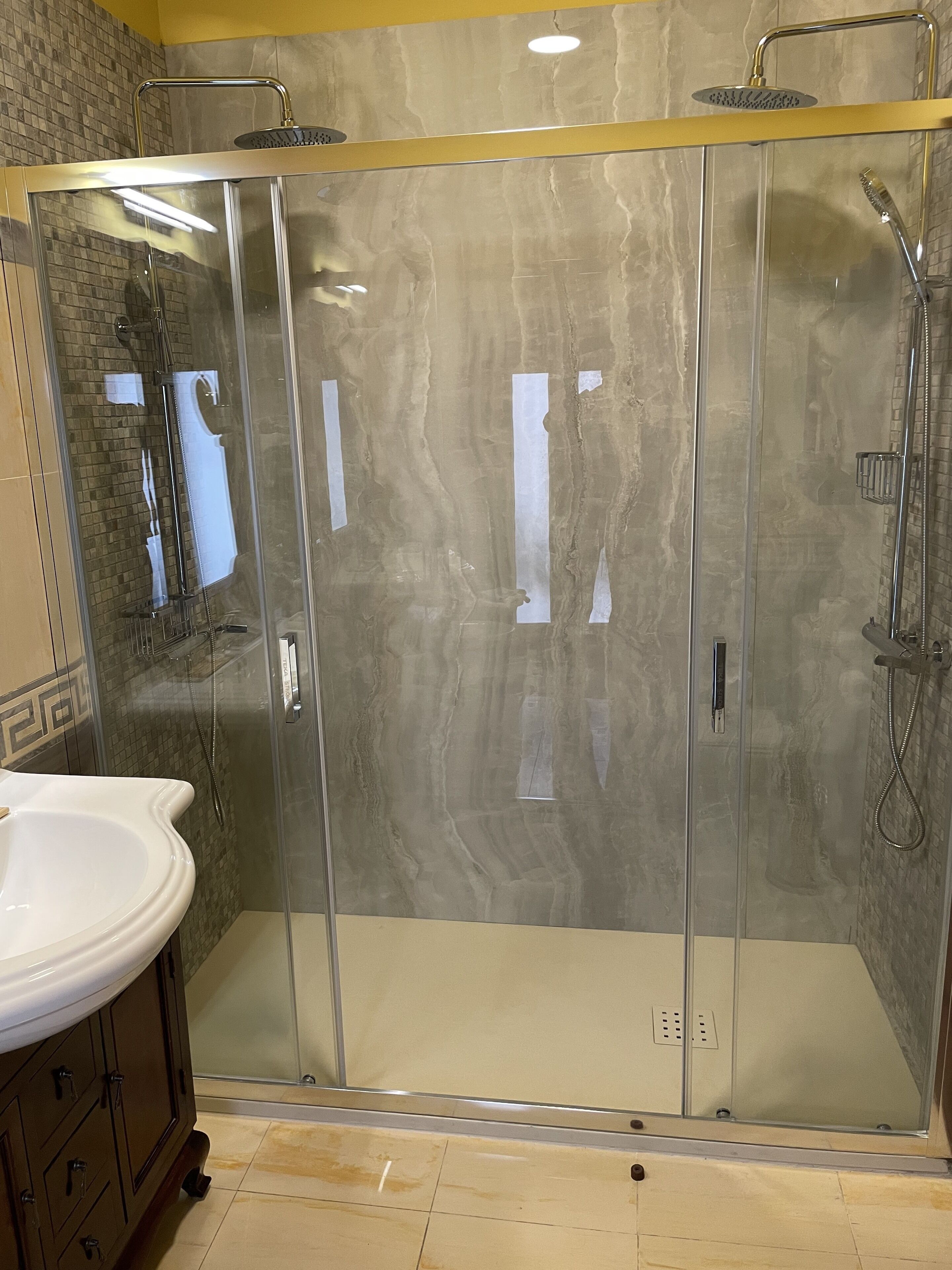 Un baño moderno con ducha de vidrio, un lavamanos blanco y suelo de baldosas de mármol.