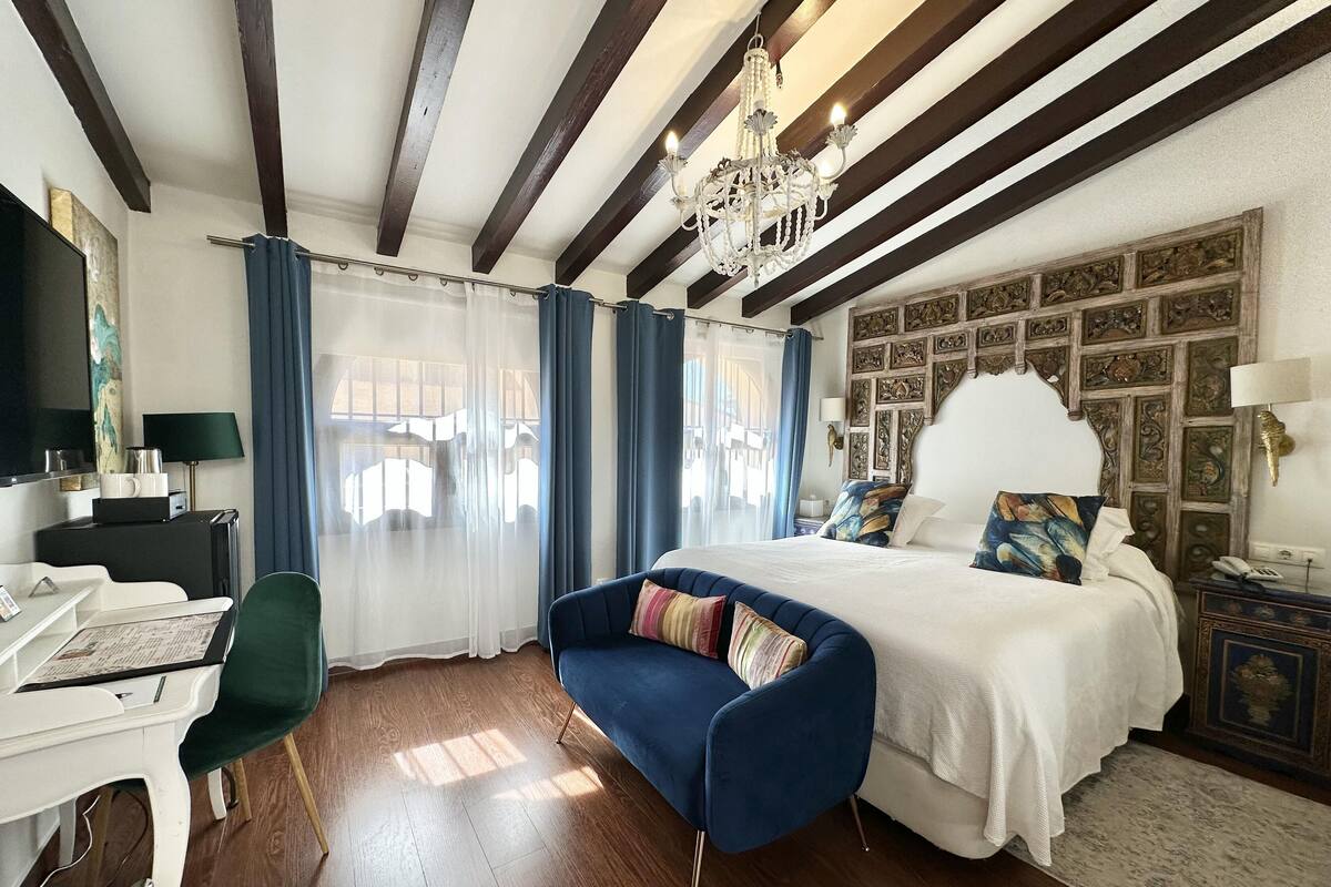 A hotel room with a large bed, a desk, a chair, a chandelier, and a decorative wall.