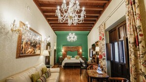 Une pièce avec un plafond en bois, un mur vert, un grand lit avec une tête de lit en bois, un lustre, un canapé, une table et des rideaux à motifs floraux.
