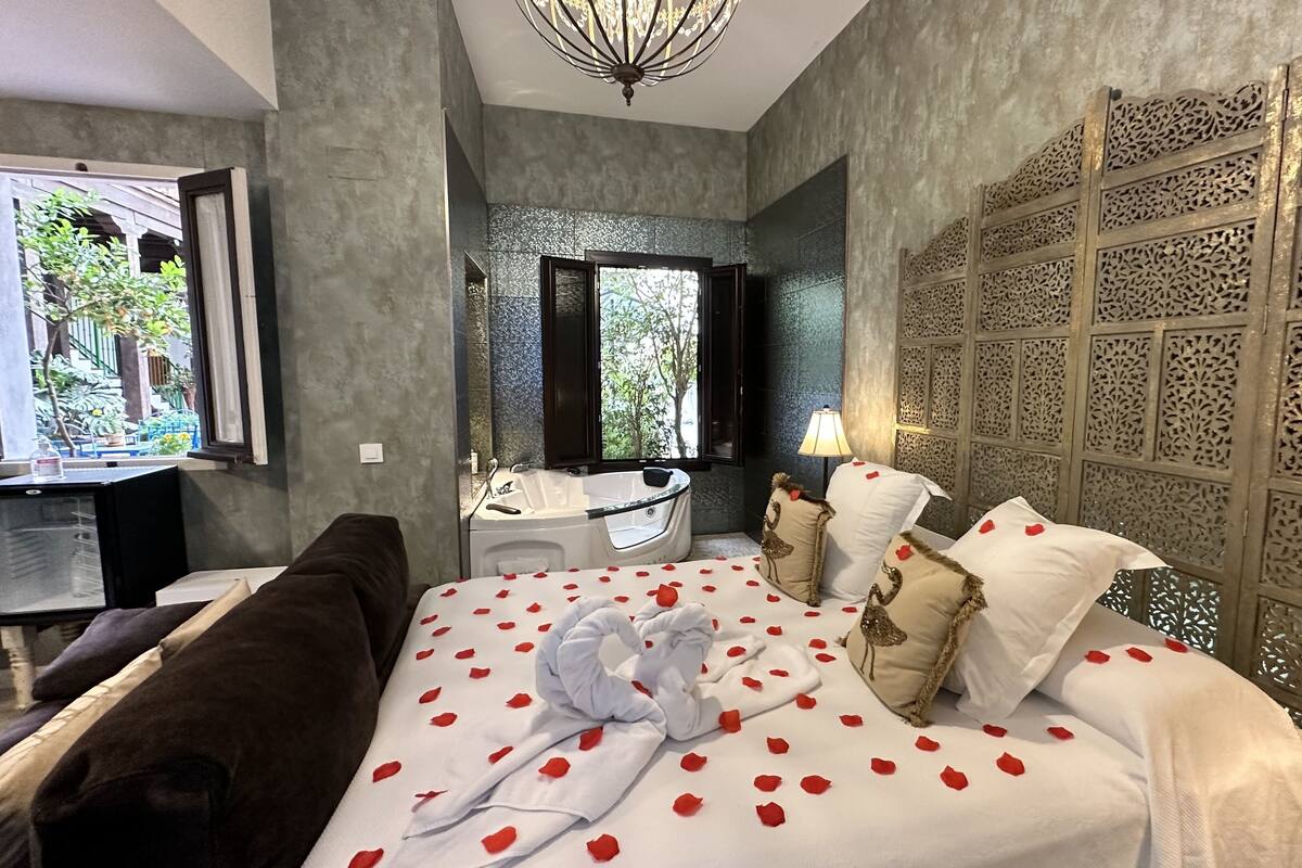 A bedroom with a bed, a bathtub, a window, and a decorative wall.