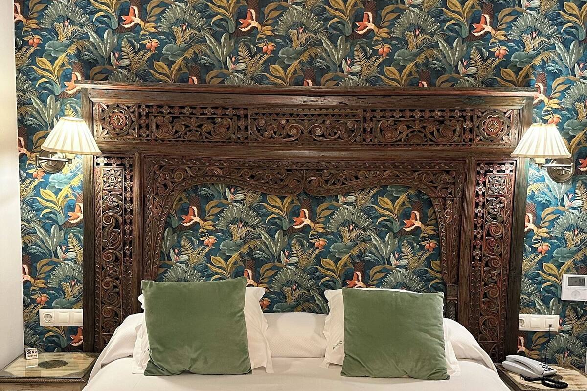 A bed with a yellow blanket, two green pillows, and a wooden headboard with intricate carvings.