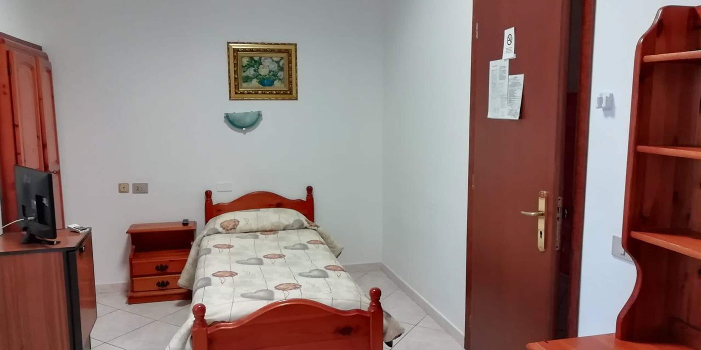 A bedroom with a bed, a dresser, a television on a cabinet, a door with a shelf, and a wall-mounted picture.
