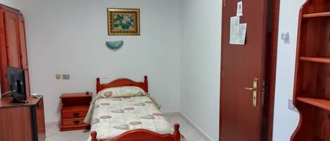 A bedroom with a bed, a dresser, a television on a cabinet, a door with a shelf, and a wall-mounted picture.