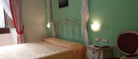 A bedroom with a bed, a nightstand, a chair, and a wall-mounted light fixture.