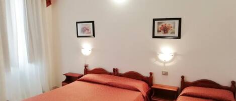 A bedroom with two wooden beds, each with a red bedspread, a nightstand, and a wall-mounted light.