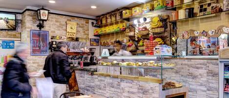 A café with a rustic brick wall, a coffee machine, and shelves stocked with jars of food and beverages.