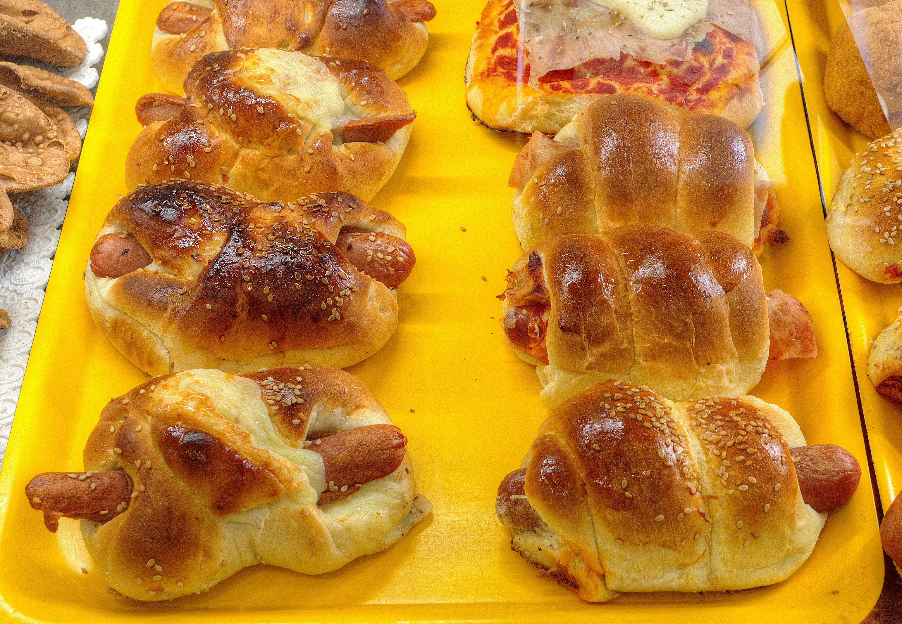 A tray of various baked goods, including bread rolls and hot dogs, on a yellow tray.