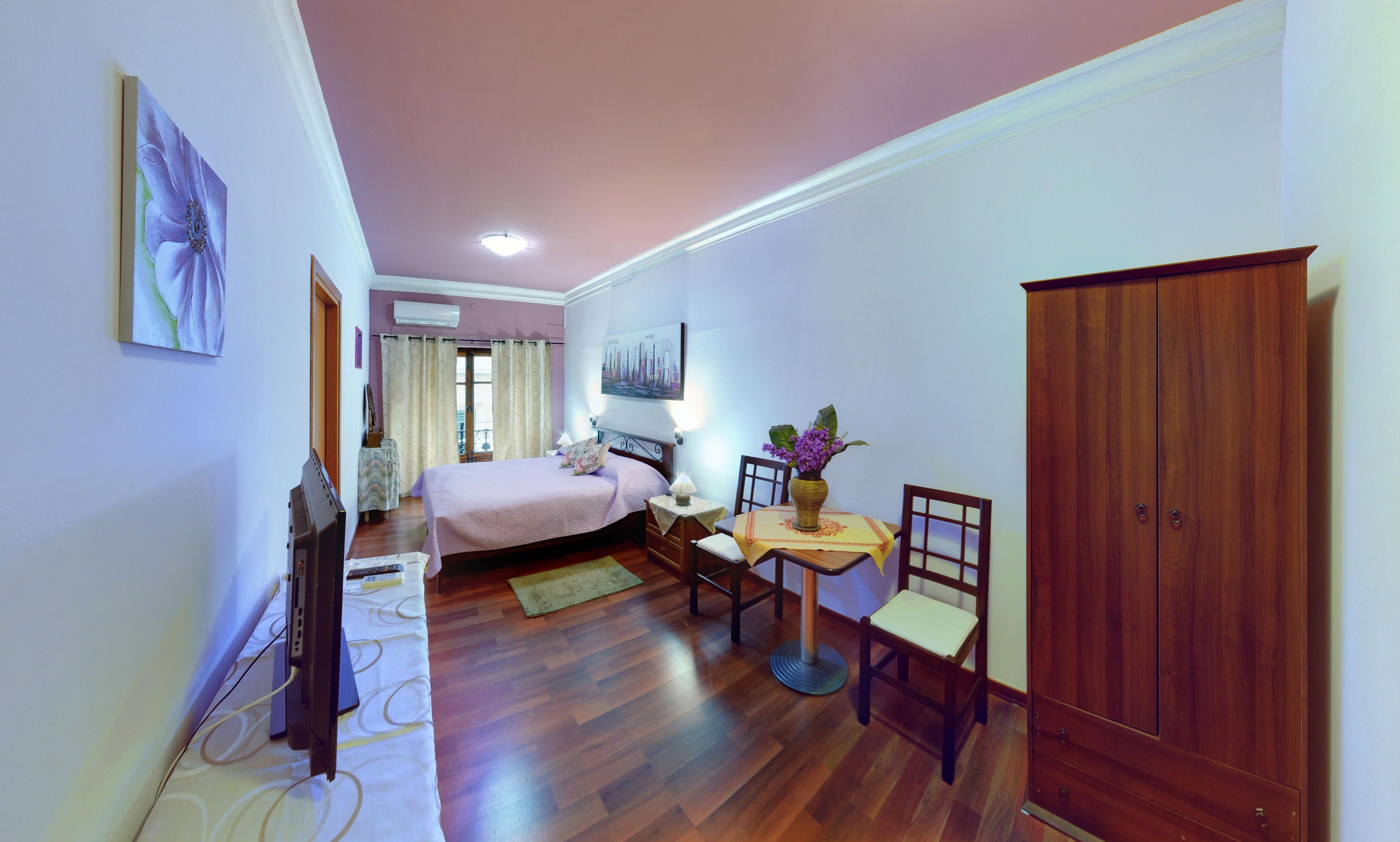 A bedroom with a bed, bedside table, chair, wardrobe, and a small table with a vase.