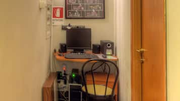 Ein schmaler Flur mit einem Holztisch, einem Computer und einem Stuhl. Eine Tür mit der Nummer 12 ist rechts zu sehen.