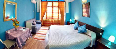 A bedroom with a bed, a sofa, a table with a vase of flowers, and a window with curtains.