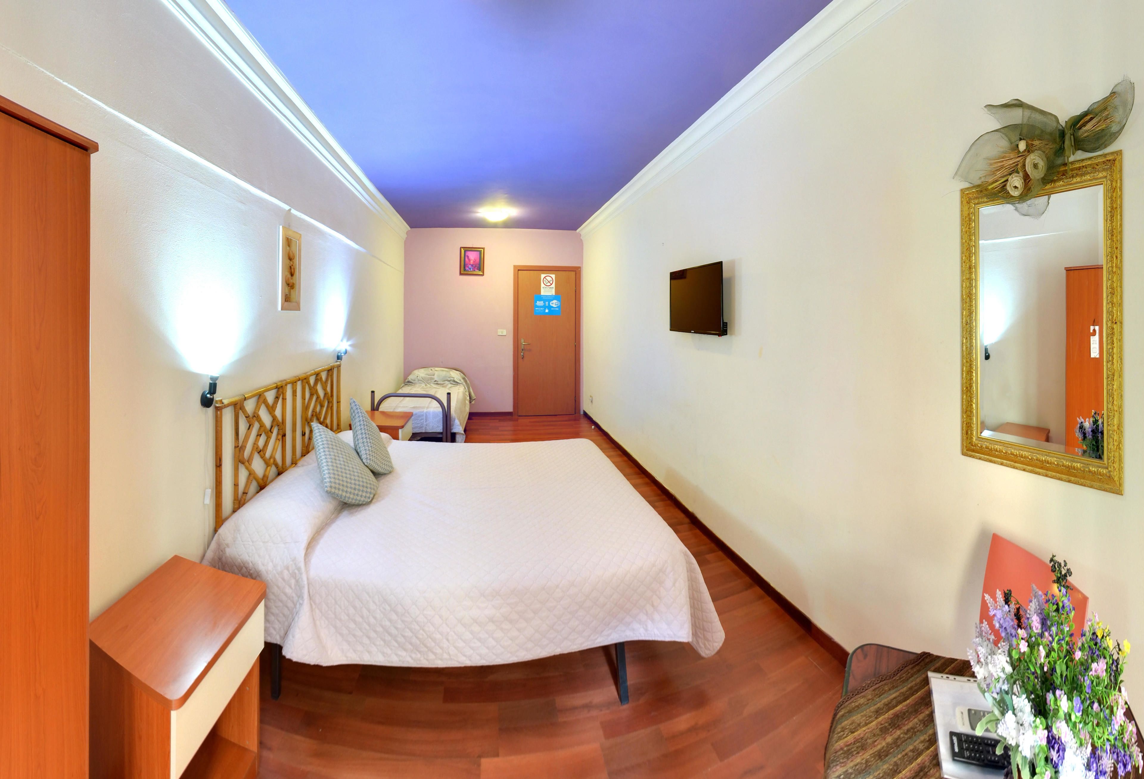 A hotel room with a bed, bedside table, and a mirror.