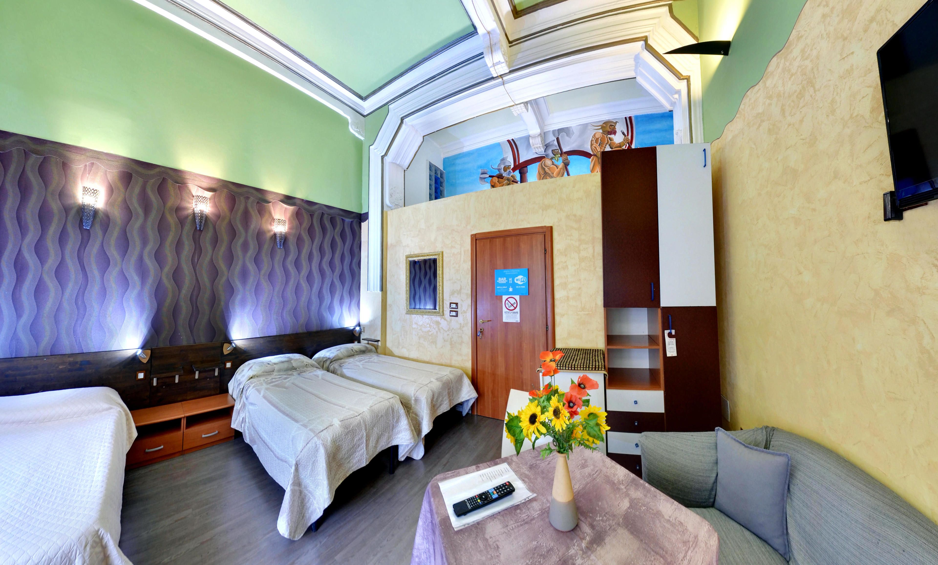 Habitación de hotel con dos camas, un sofá, una mesita con un florero y una puerta con un cartel que indica bar y Wi-Fi.