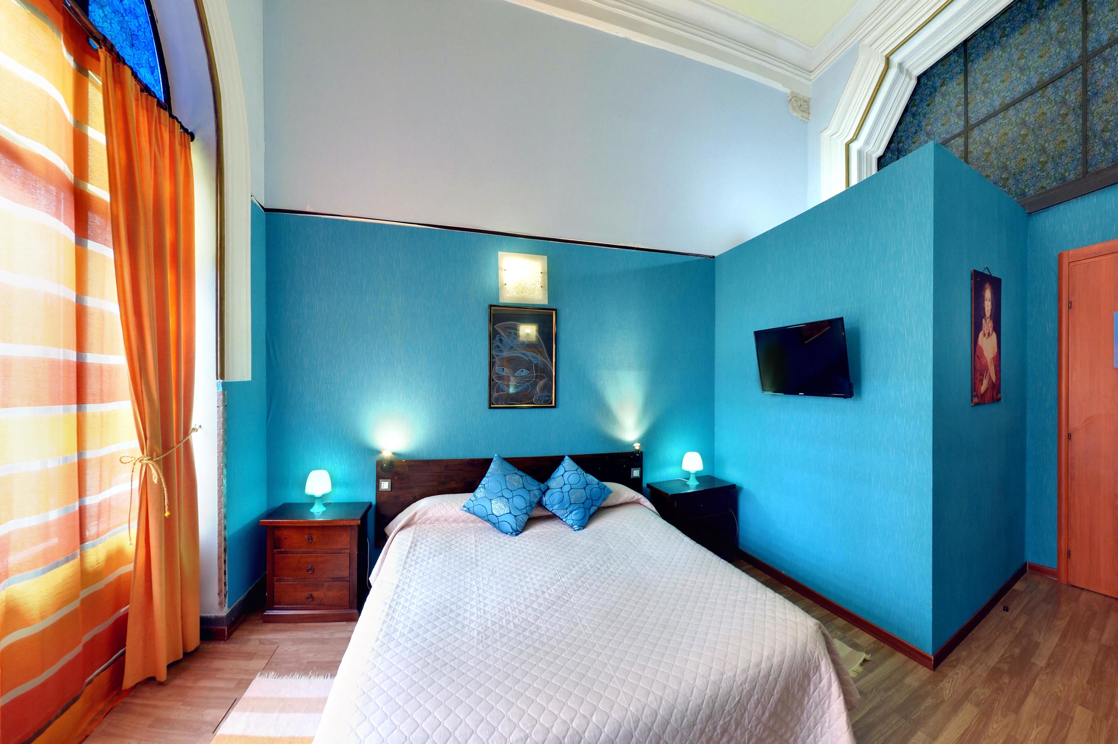 Een slaapkamer met een bed, twee nachtkastjes met lampen, een aan de muur bevestigde televisie en een deur.