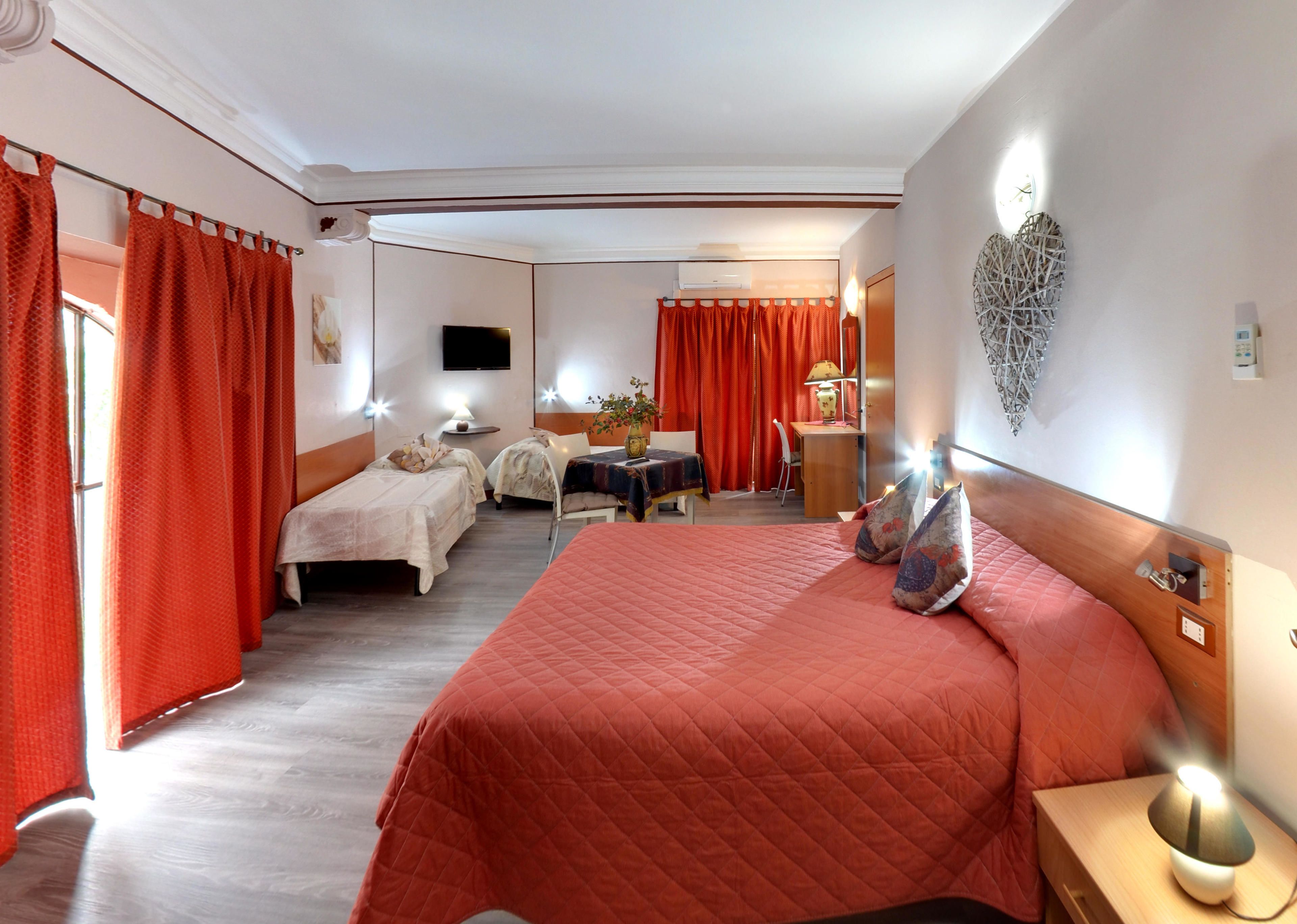 A hotel room with a large bed, two smaller beds, a desk, a chair, and a TV.
