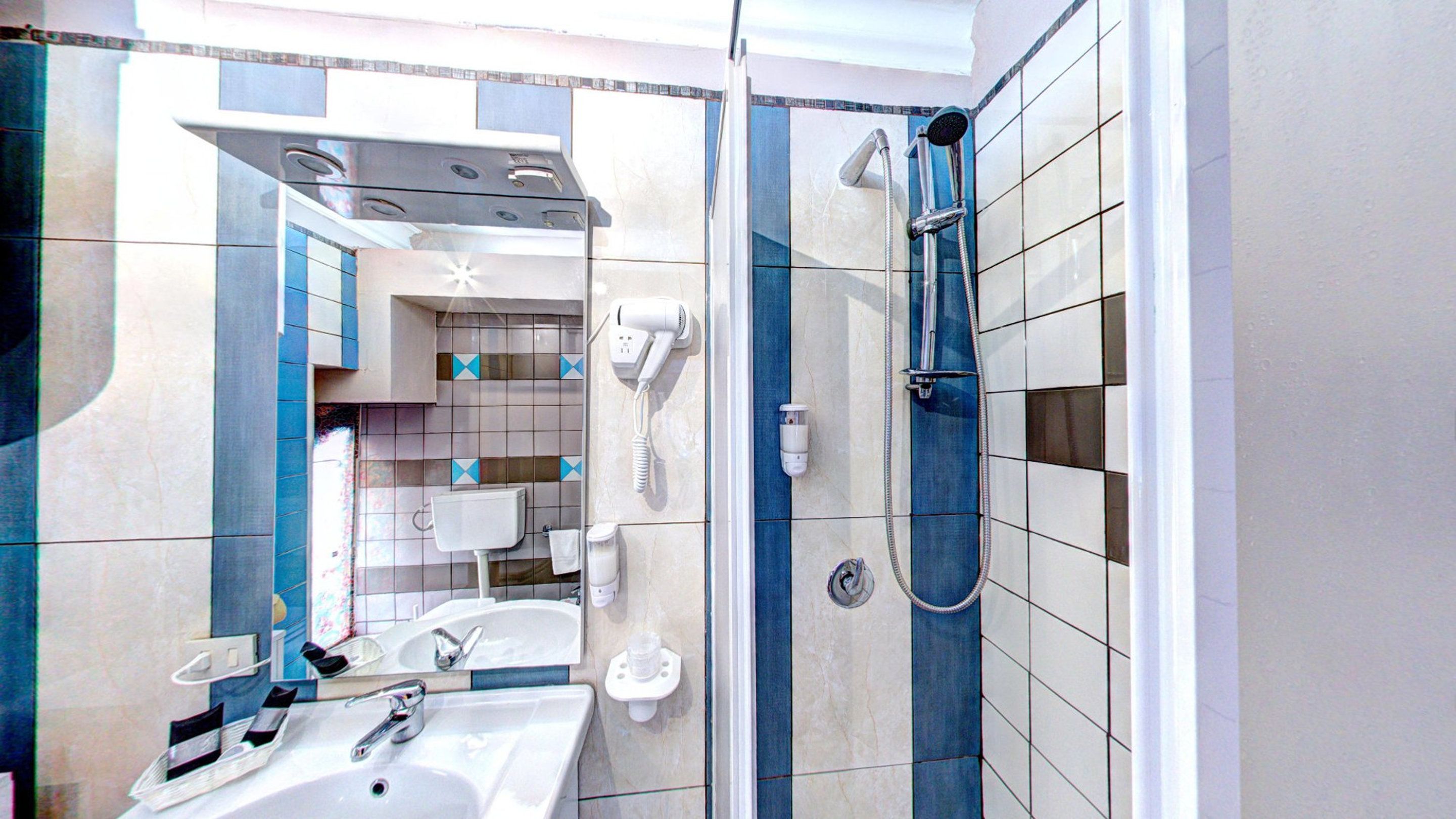 Un bagno con lavandino, specchio, portasciugamani e doccia dotata di soffione manuale.