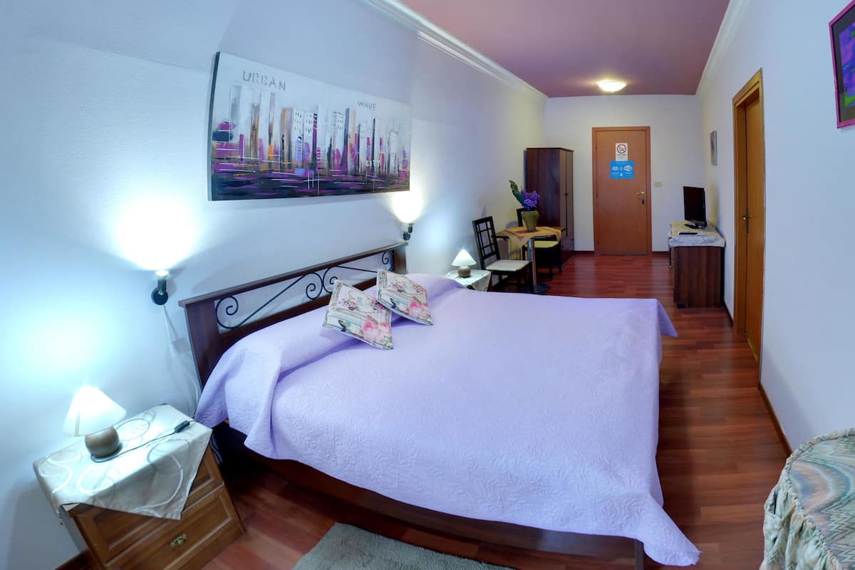 A bedroom with a bed, bedside table, lamp, and a painting on the wall.