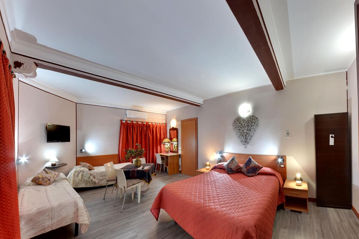A hotel room with a large bed, two smaller beds, a desk, a chair, and a TV.