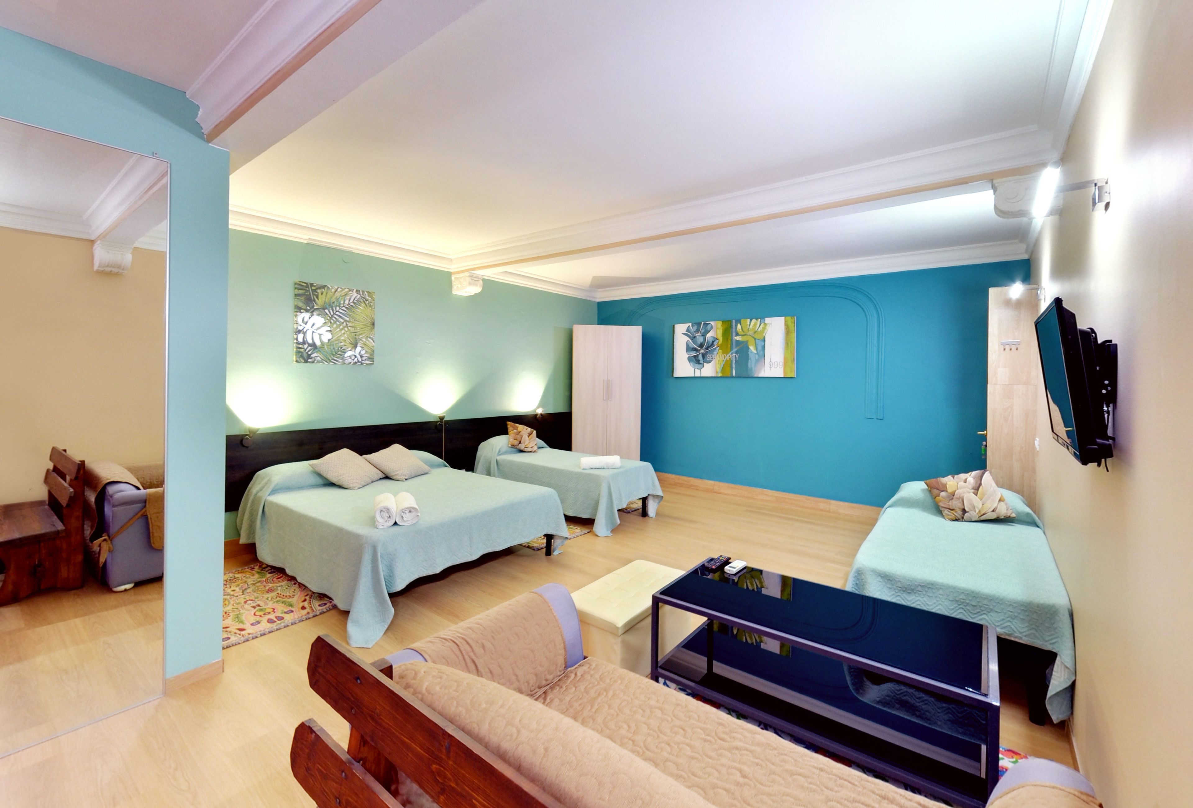 A hotel room with two beds, a sofa, a TV, and artwork on the walls.