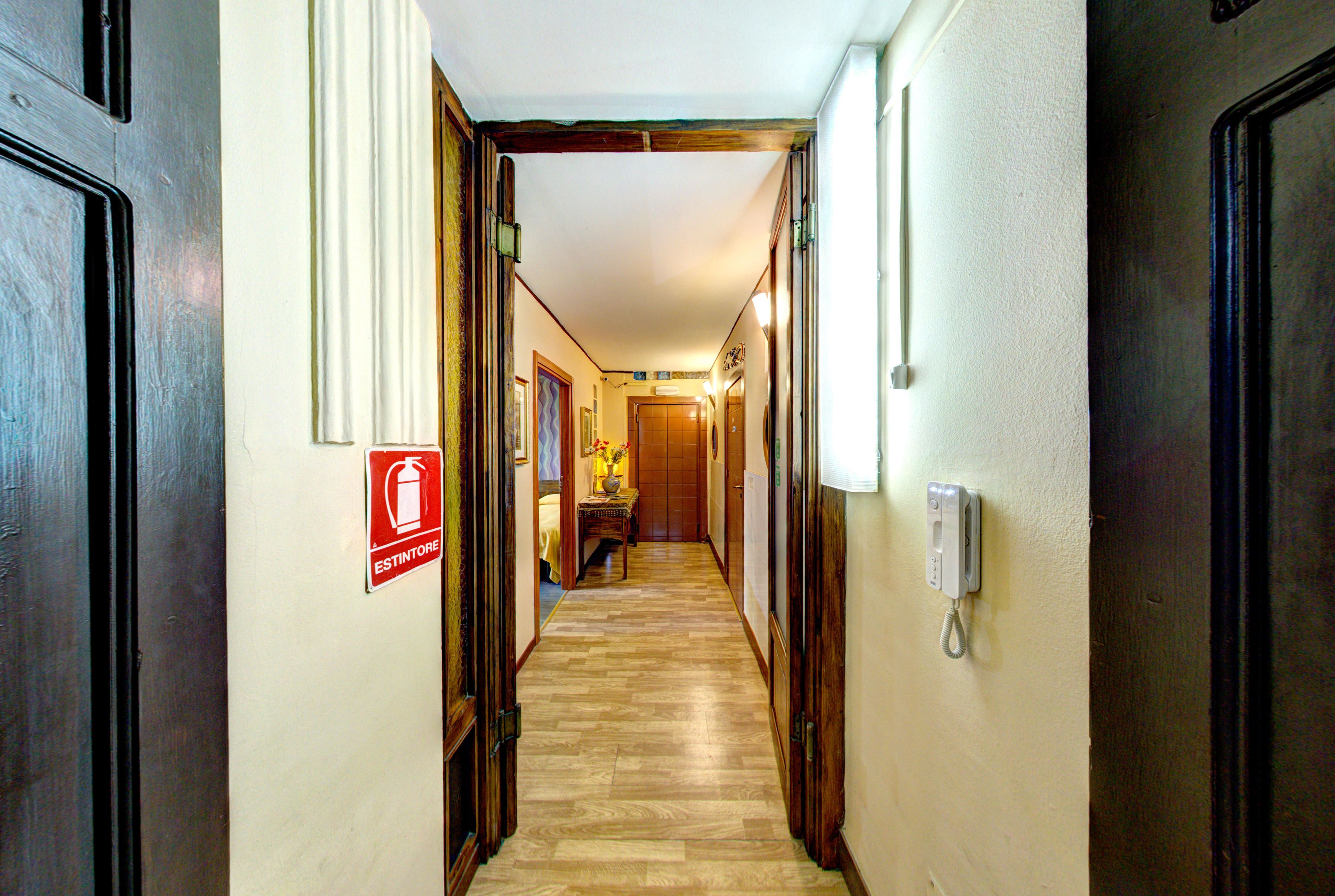 A hotel hallway with wooden floors, a fire extinguisher sign, a telephone, and a door at the end.