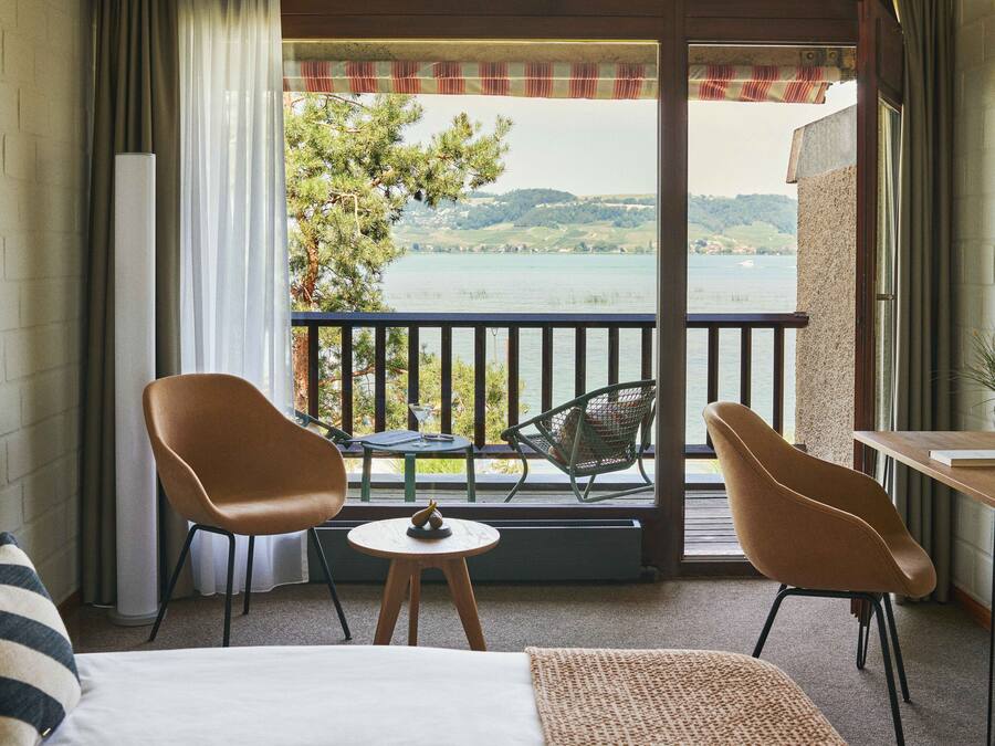 A balcony with a view of a lake and hills, furnished with two chairs and a small table.