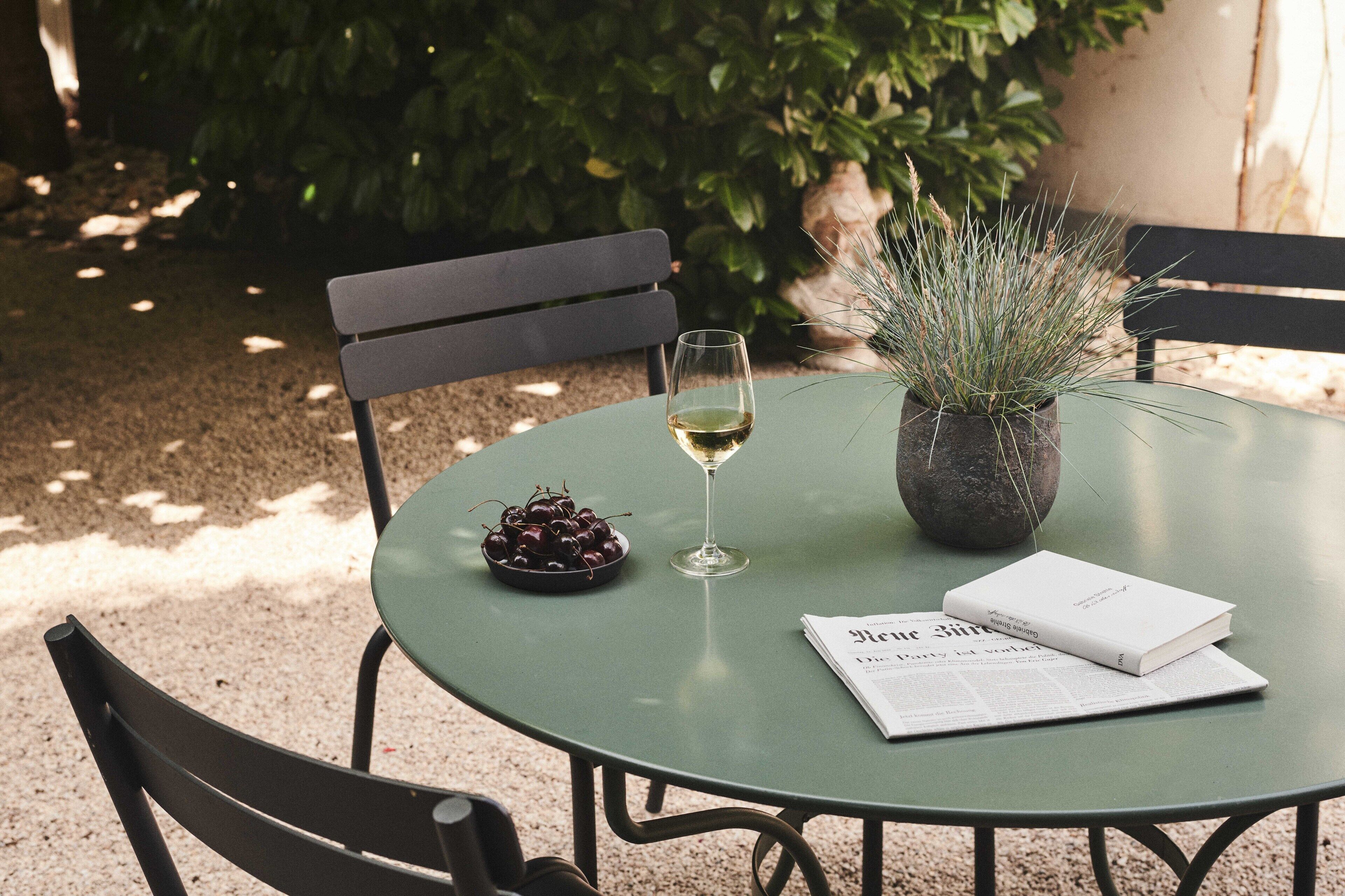 Une table ronde avec un livre, un verre de vin blanc et un bol de cerises.