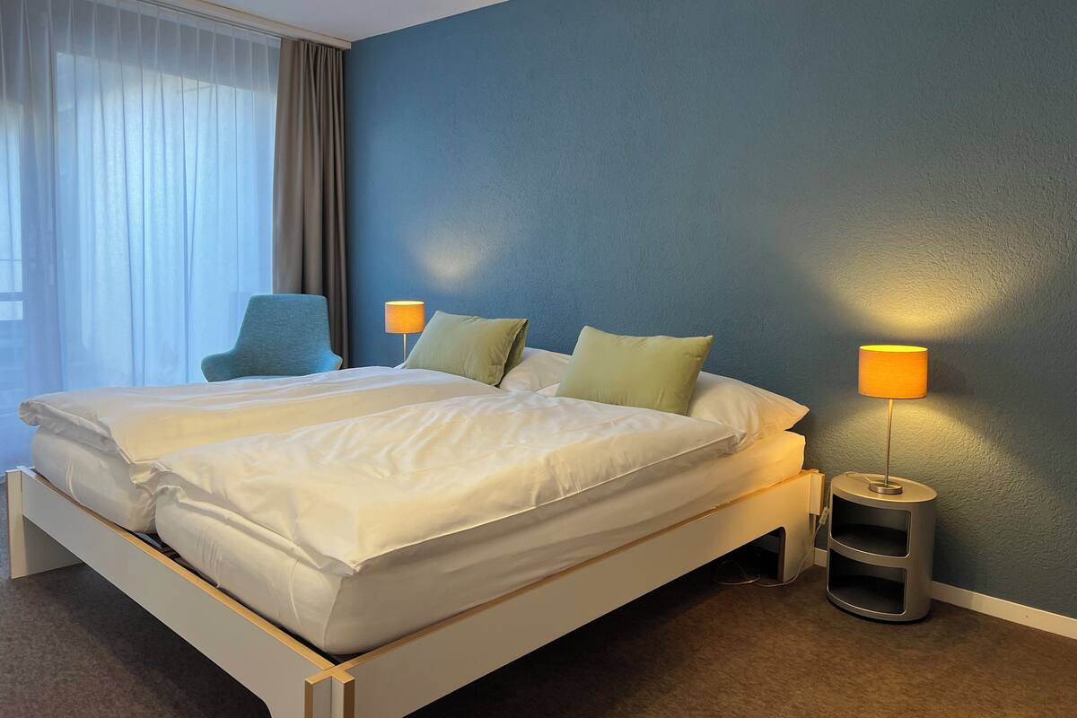 Una cama doble con sábanas blancas, dos lámparas de noche y una pared azul.