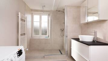 A modern bathroom with a walk-in shower, a large window, a sink, and a washing machine.