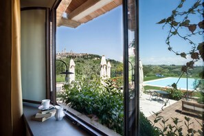 Vista desde una ventana a una piscina, follaje y un edificio distante.