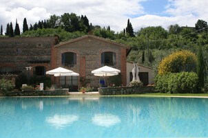 Area piscina con edificio in pietra, due ombrelloni e una statua.