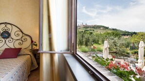 Un dormitorio con un amplio ventanal que da a un jardín y una vista distante de una colina con edificios.