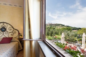 Una camera da letto con un'ampia finestra vista giardino e una collinetta con edifici in lontananza.